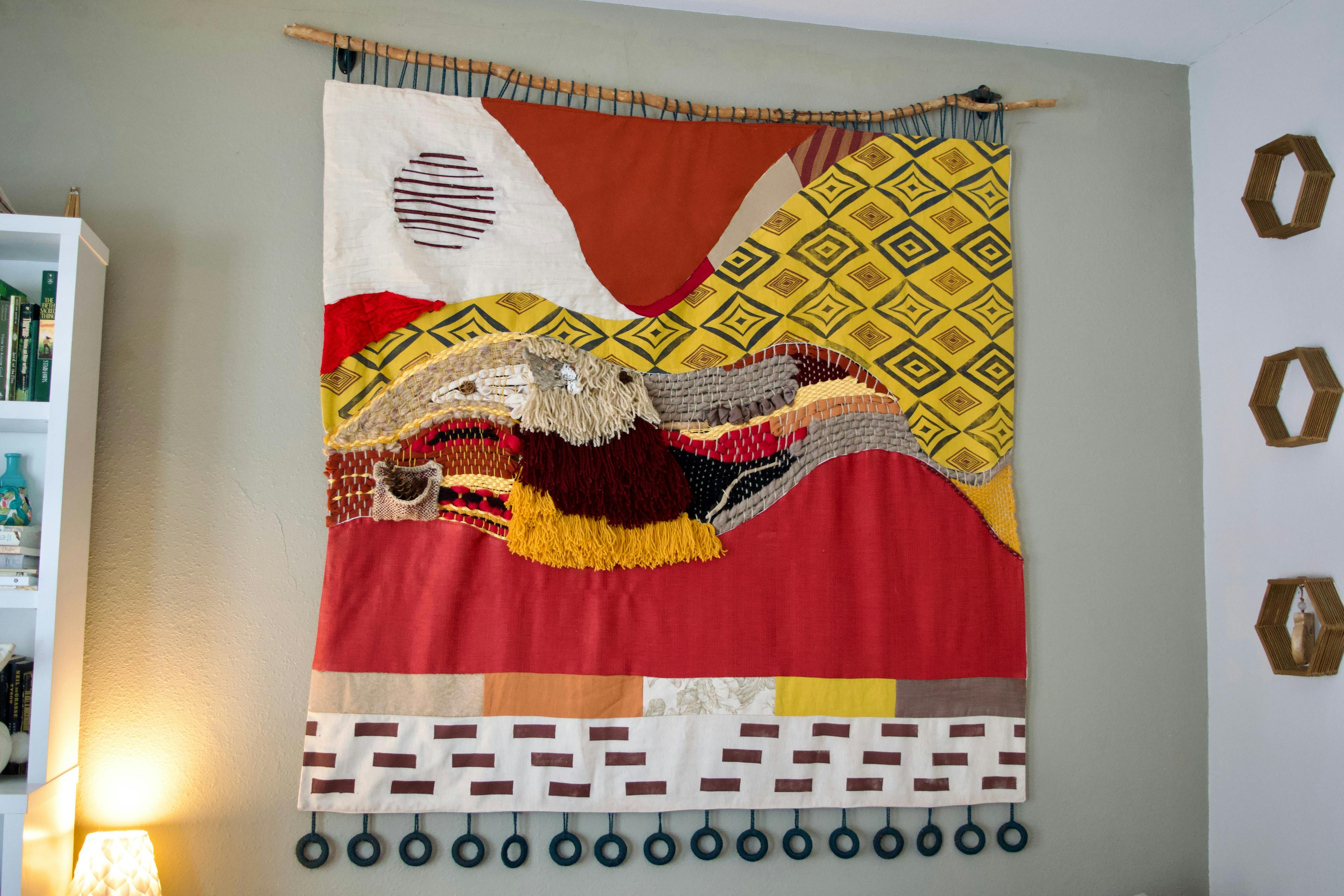 A huge red, yellow, cream, and brown wall hanging made of yarn and fabric.