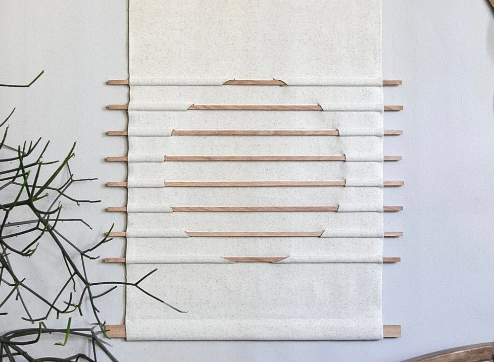 A white fabric wall hanging with small threaded through in the shape of a circle.