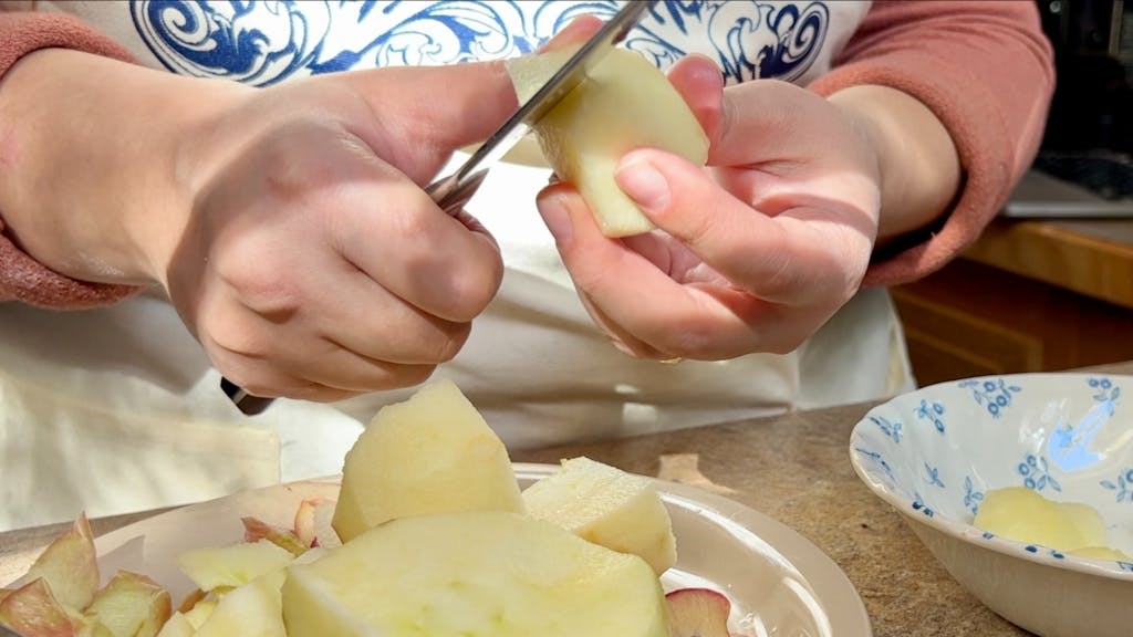 Carving a raw apple into small spheres with a knife.