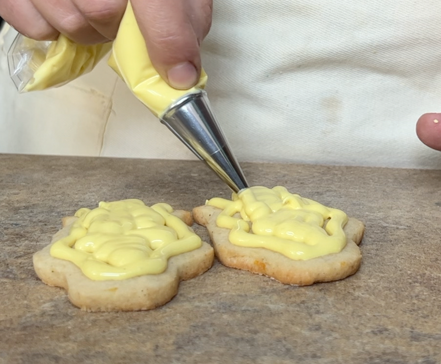 Piping yellow icing onto a cookie