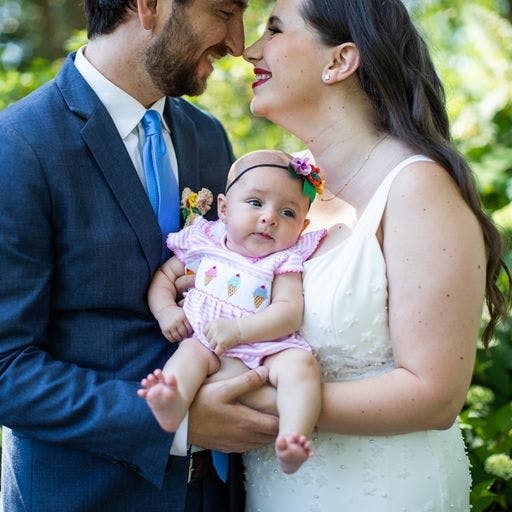 Lauren and Jake touching noses while they hold Rhea. She is wearing her headband and a pink onesie with ice cream cones on it.