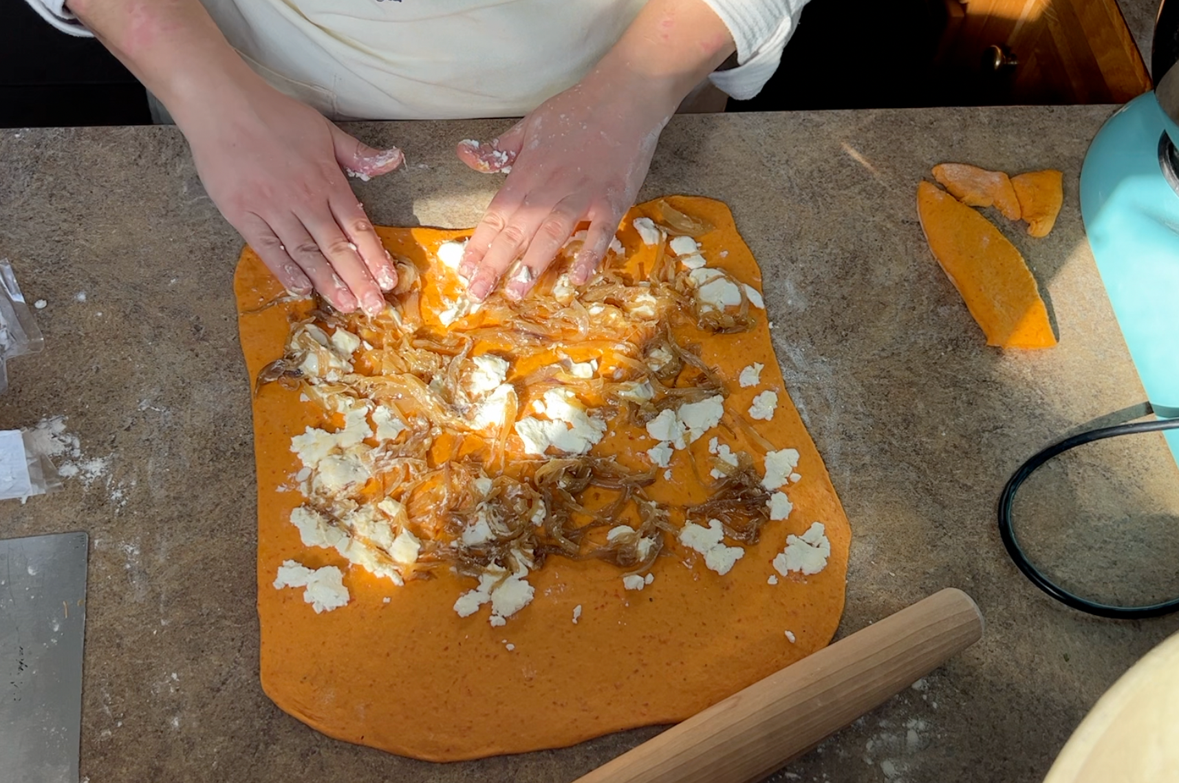 Laying goat cheese and caramelized onions onto a square of orange dough