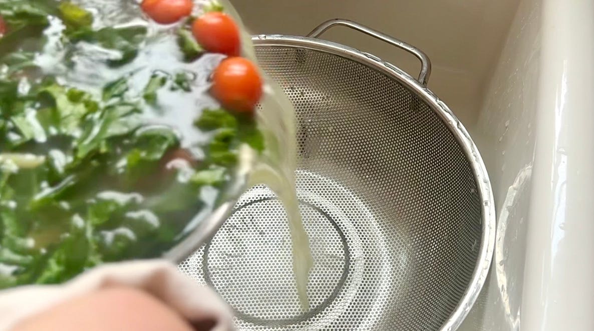 A pot of kale, tomatoes, and pasta being poured into a colander.