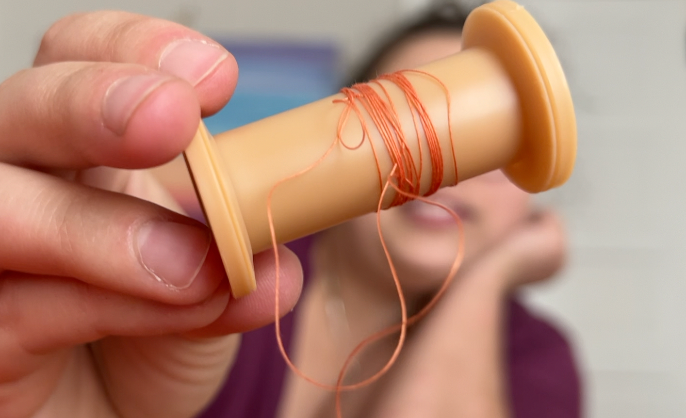 A spool of thread with very little orange thread left on it