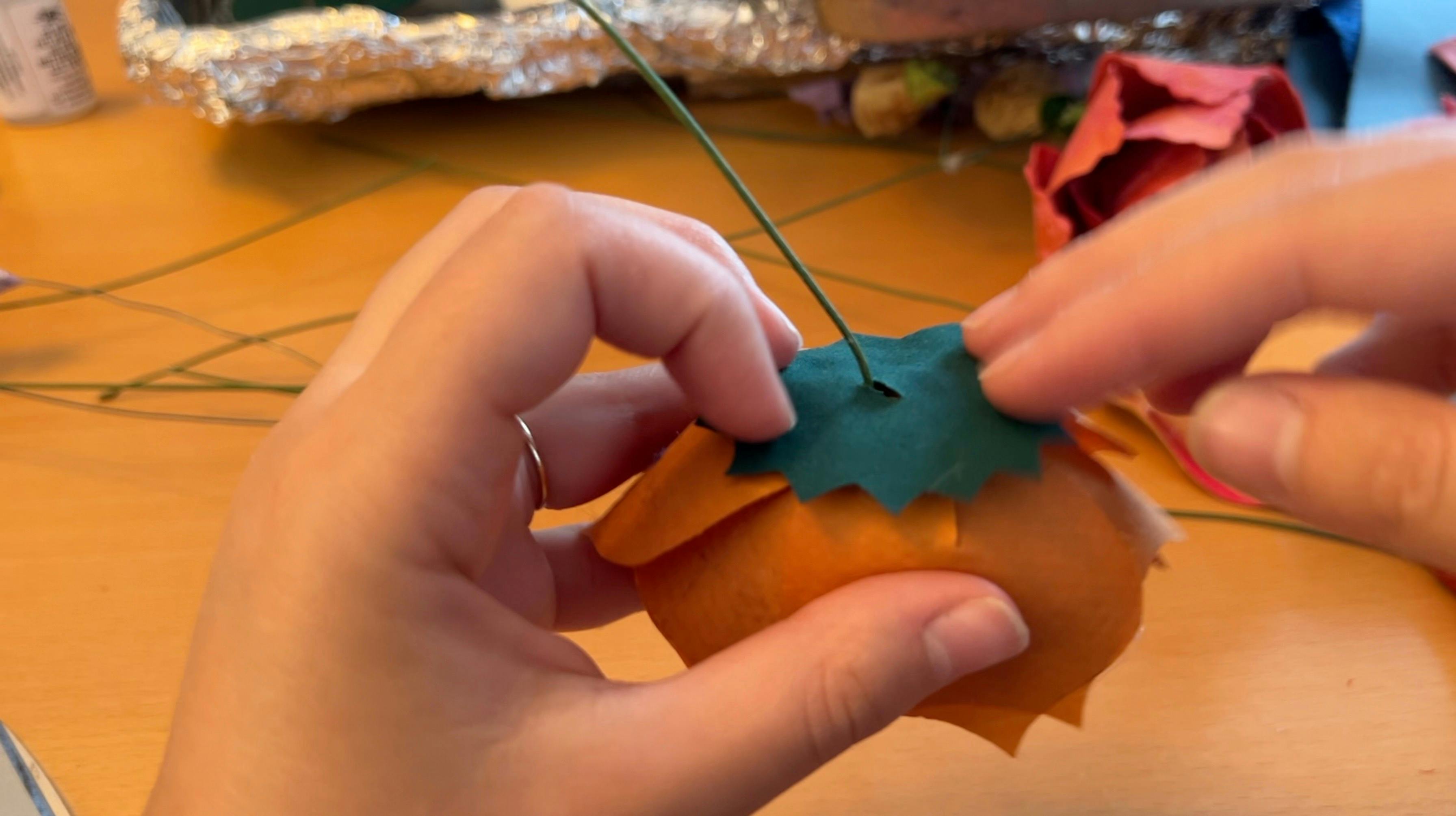 Gluing a green pointy circle on the bottom of an orange flower.