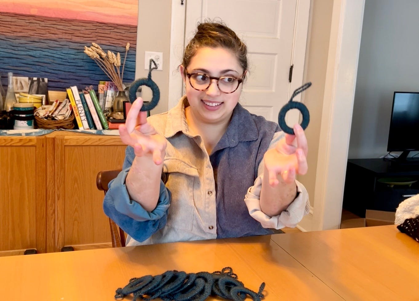 Holding up two yarn covered rings and smiling