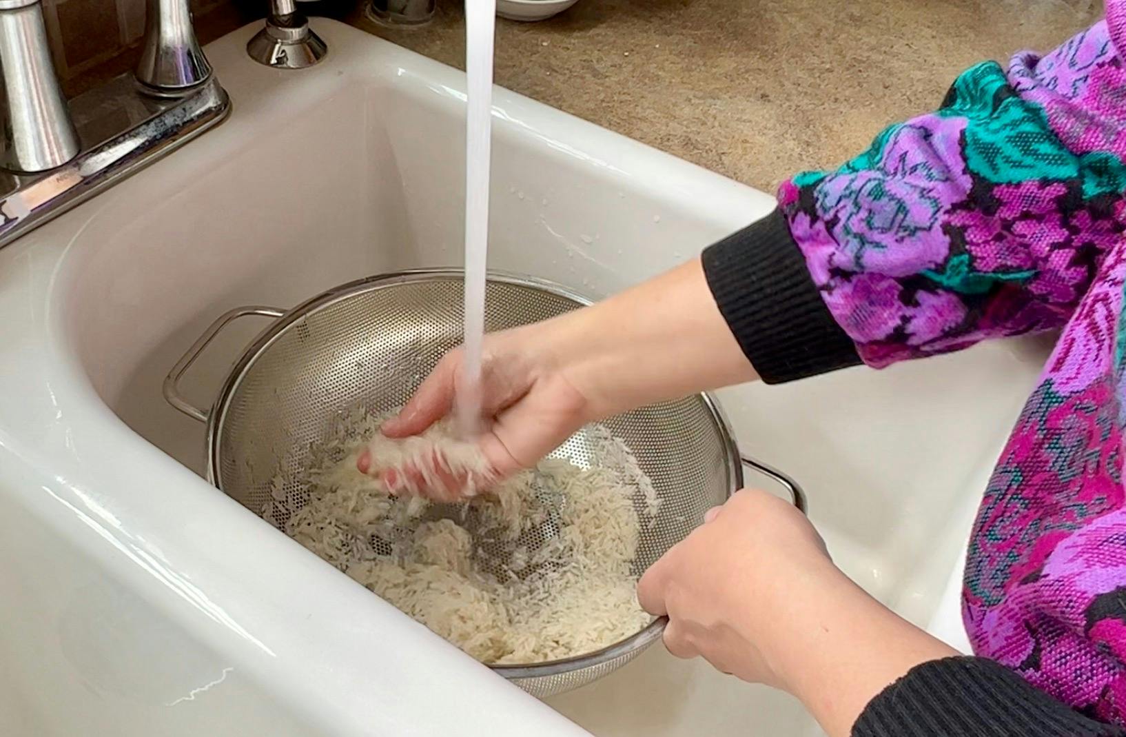 Washing rice in a colander in the sink.