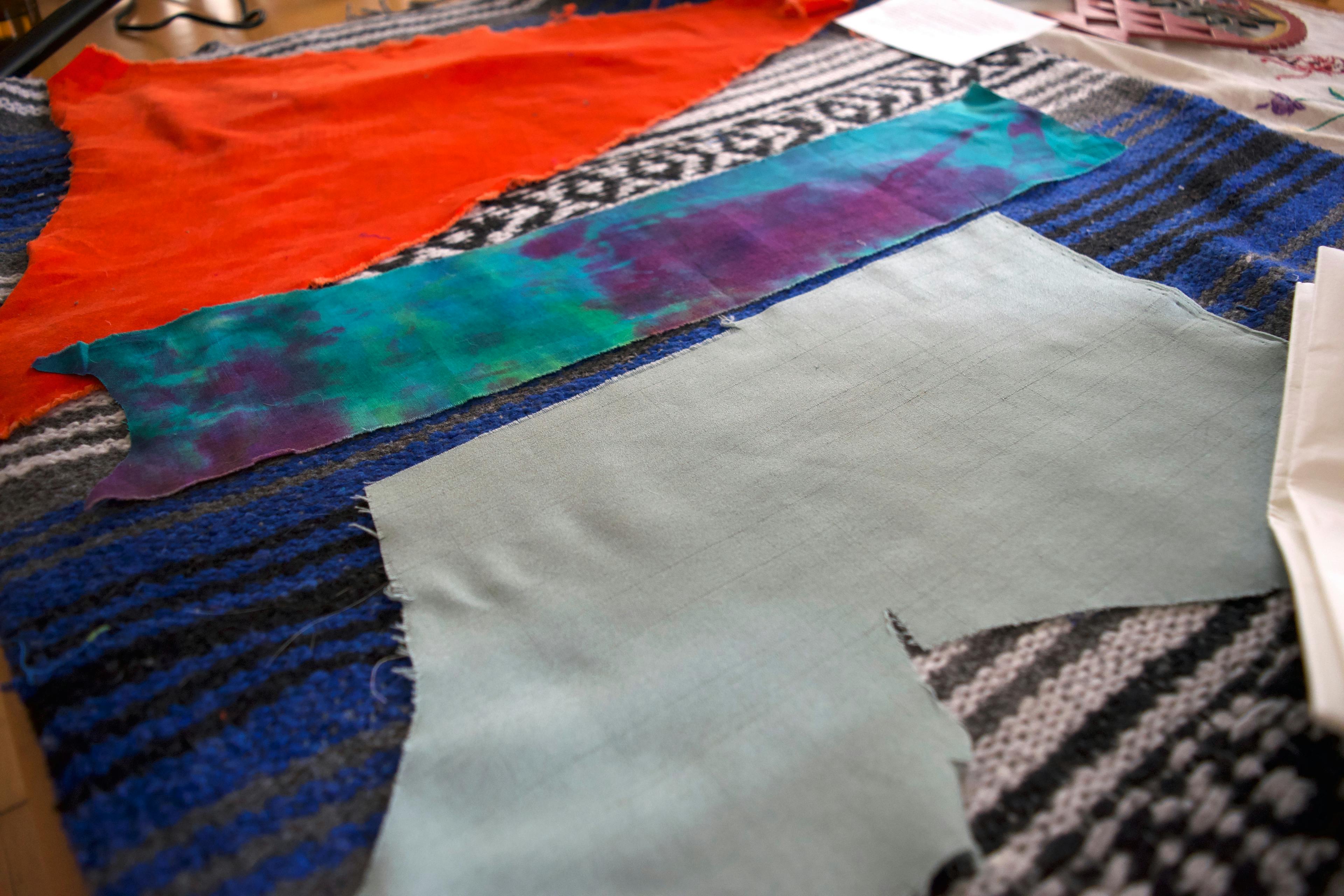 Three fabrics are laid out on Katrina's ironing surface, which is a blue yoga blanket. There is an orange velvet, a hand dyed blue and purple and green cotton, and a light blue thin fabric.