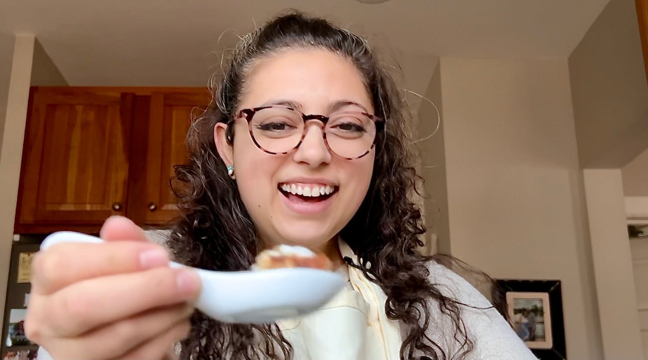 Katrina (smiling) with a bite sized piece of cake in a ramen spoon.