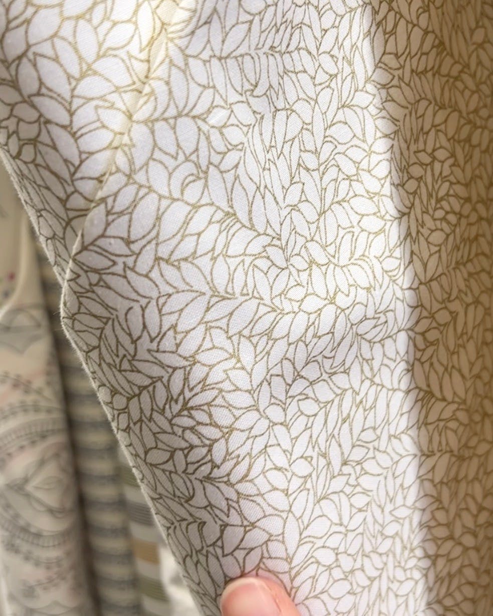 White and gold leaf fabric on the shelf at a fabric store.