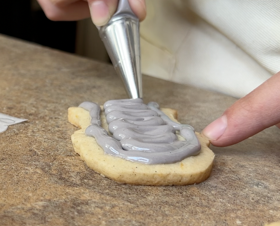 Piping grey icing onto a cookie