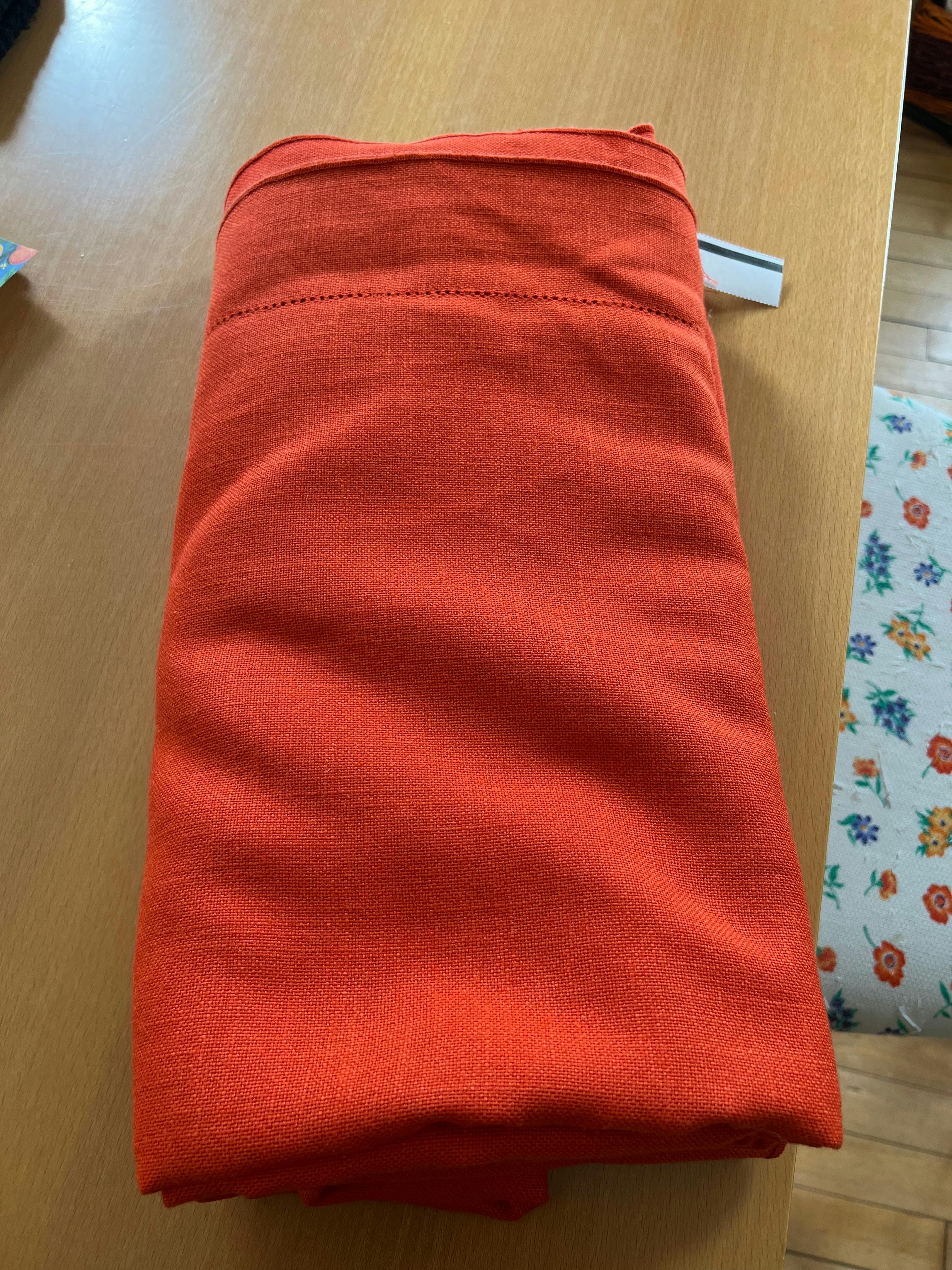 A folded up orange tablecloth with the thrift store price tag still showing