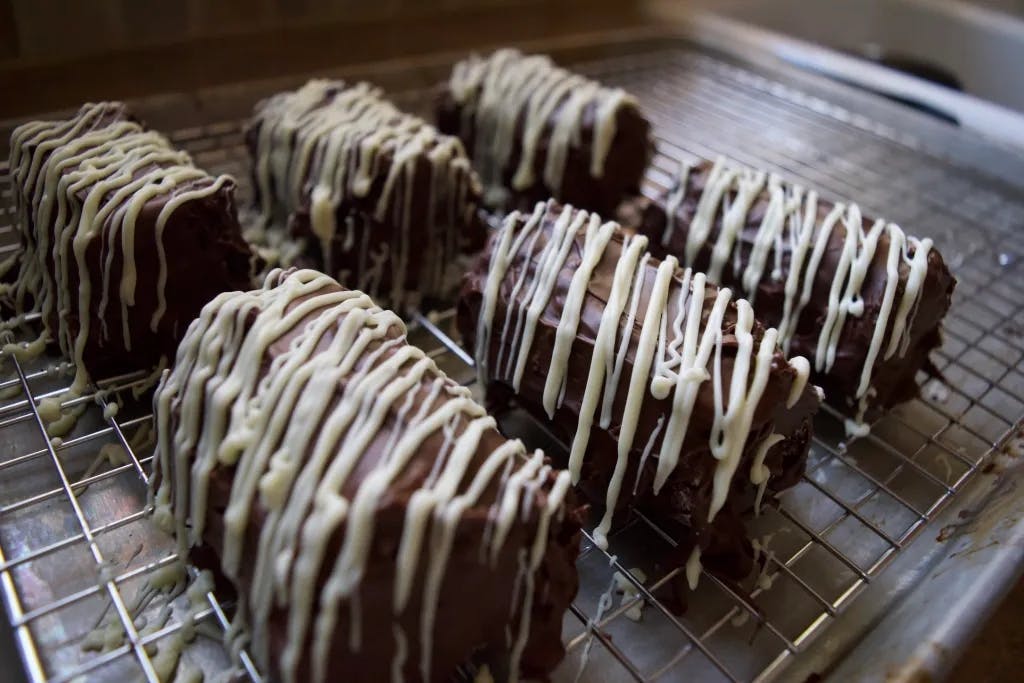 Close up of dark chocolate covered mini cake rolls with white chocolate drizzled diagonally.