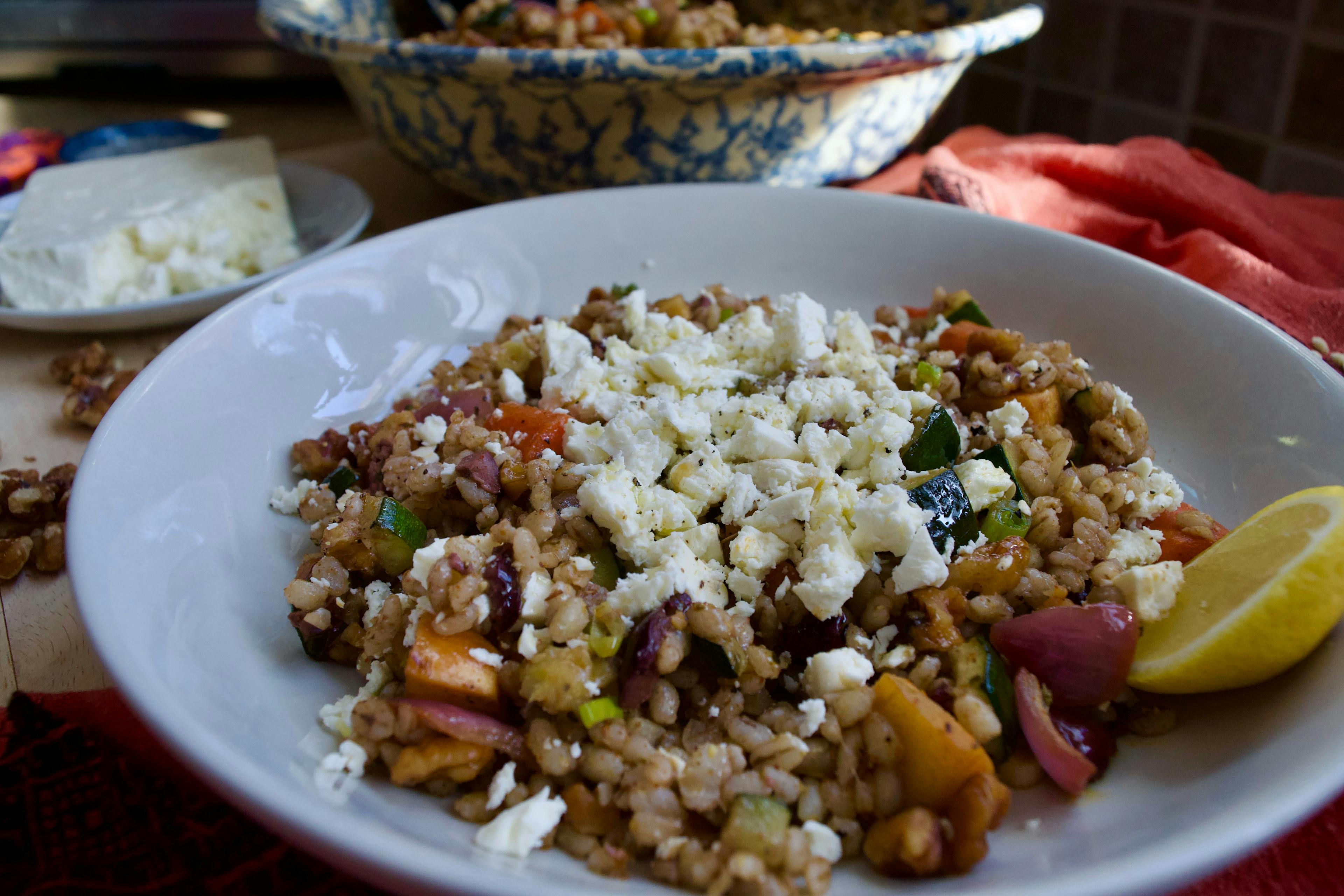 A plate of barley salad with crumbled feta and a lemon wedge on the side.