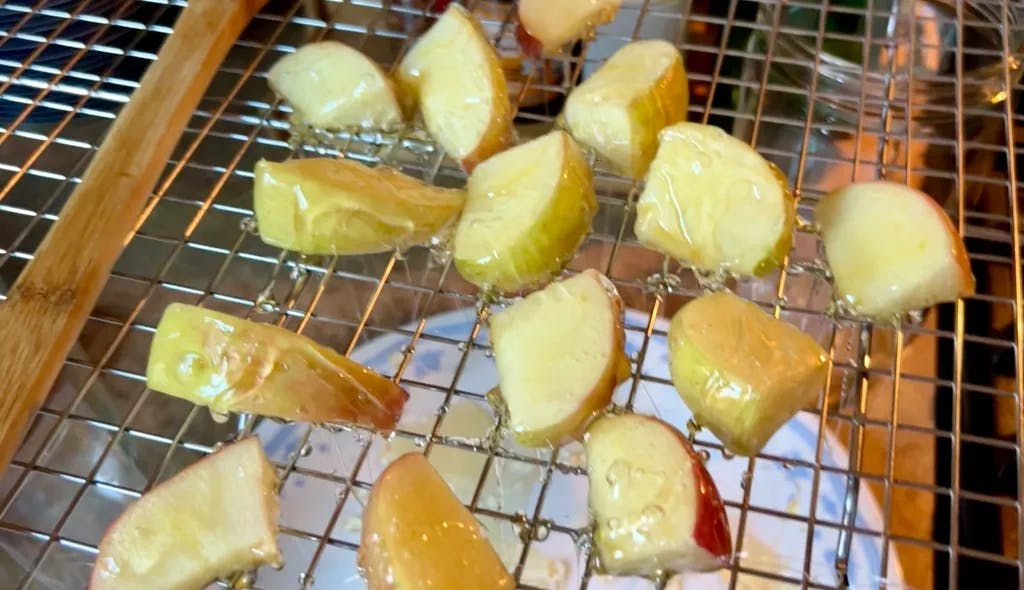 Pieces of apple dipped in caramel that is too light, on a wire rack.