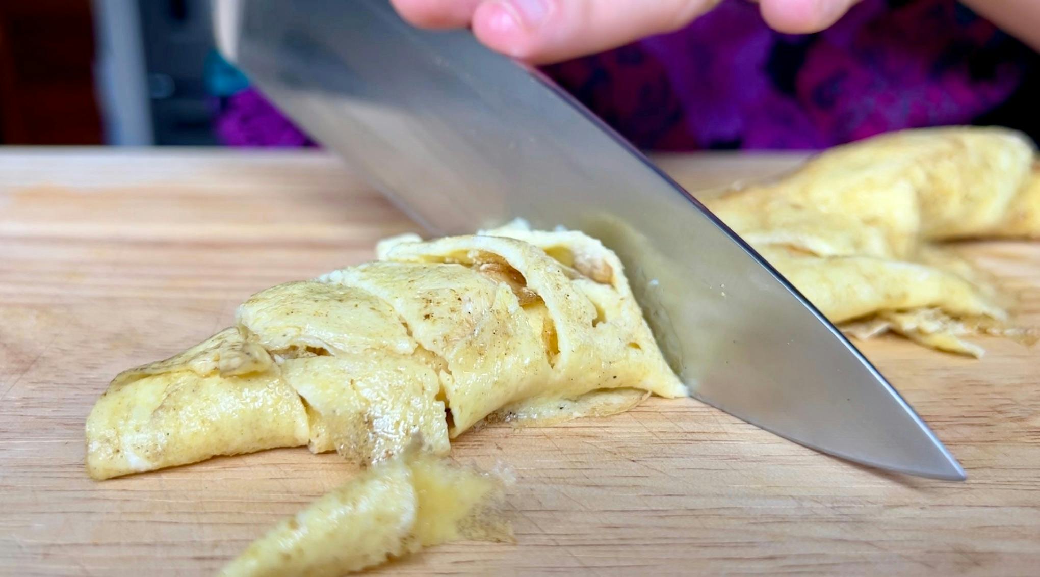 A thin omelette being cut into strips.