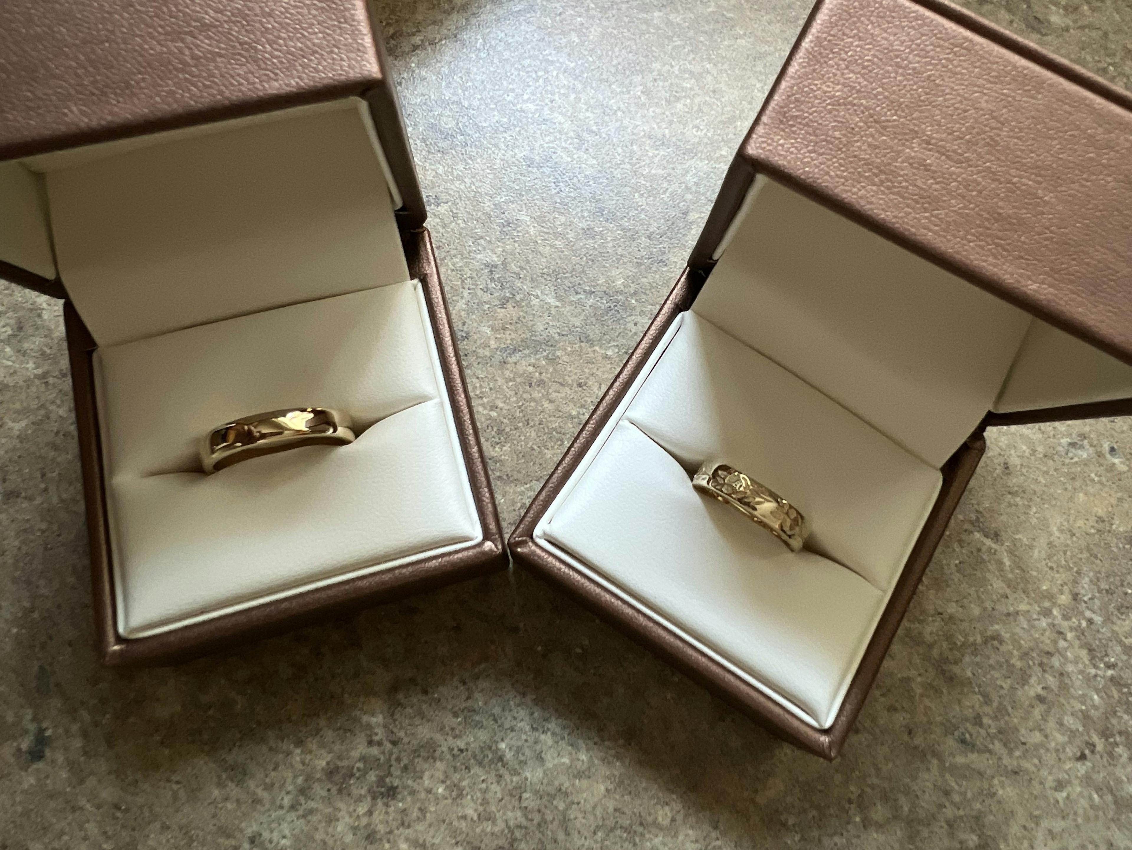 Two gold wedding rings in brown boxes.