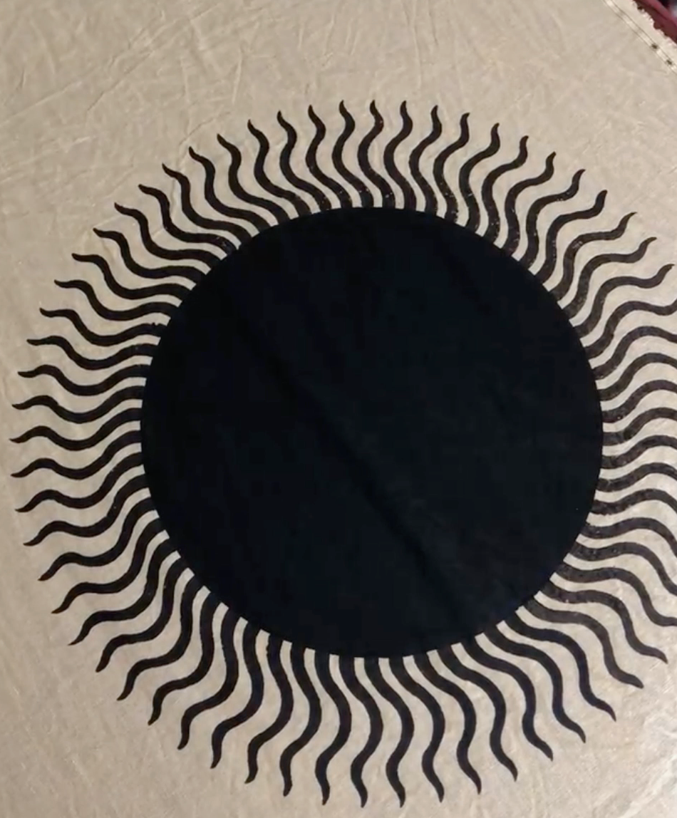 A block printed sun with wiggly rays. The sun is black on cream fabric.