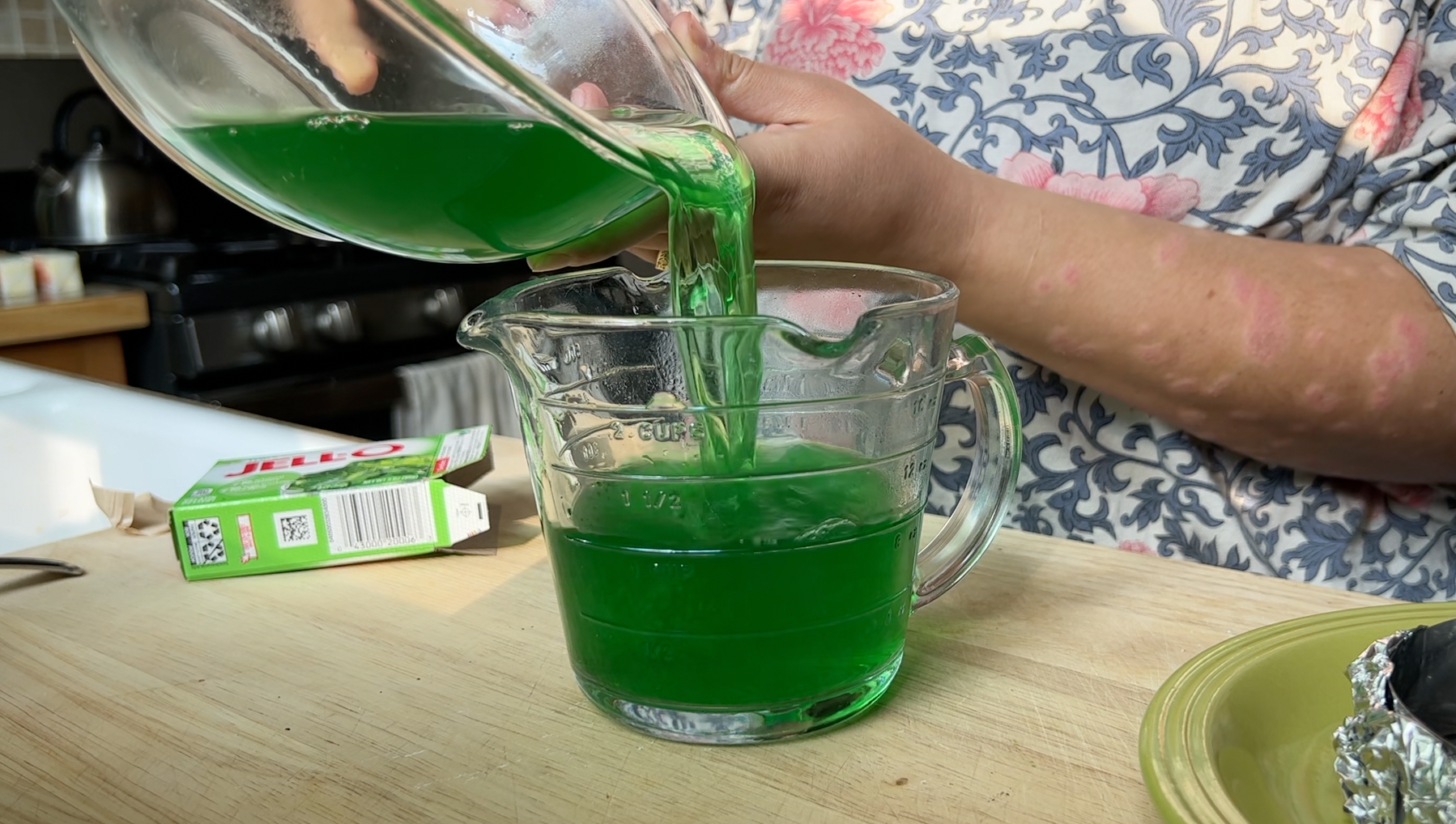 Pouring green jello mix into a clear glass measuring cup