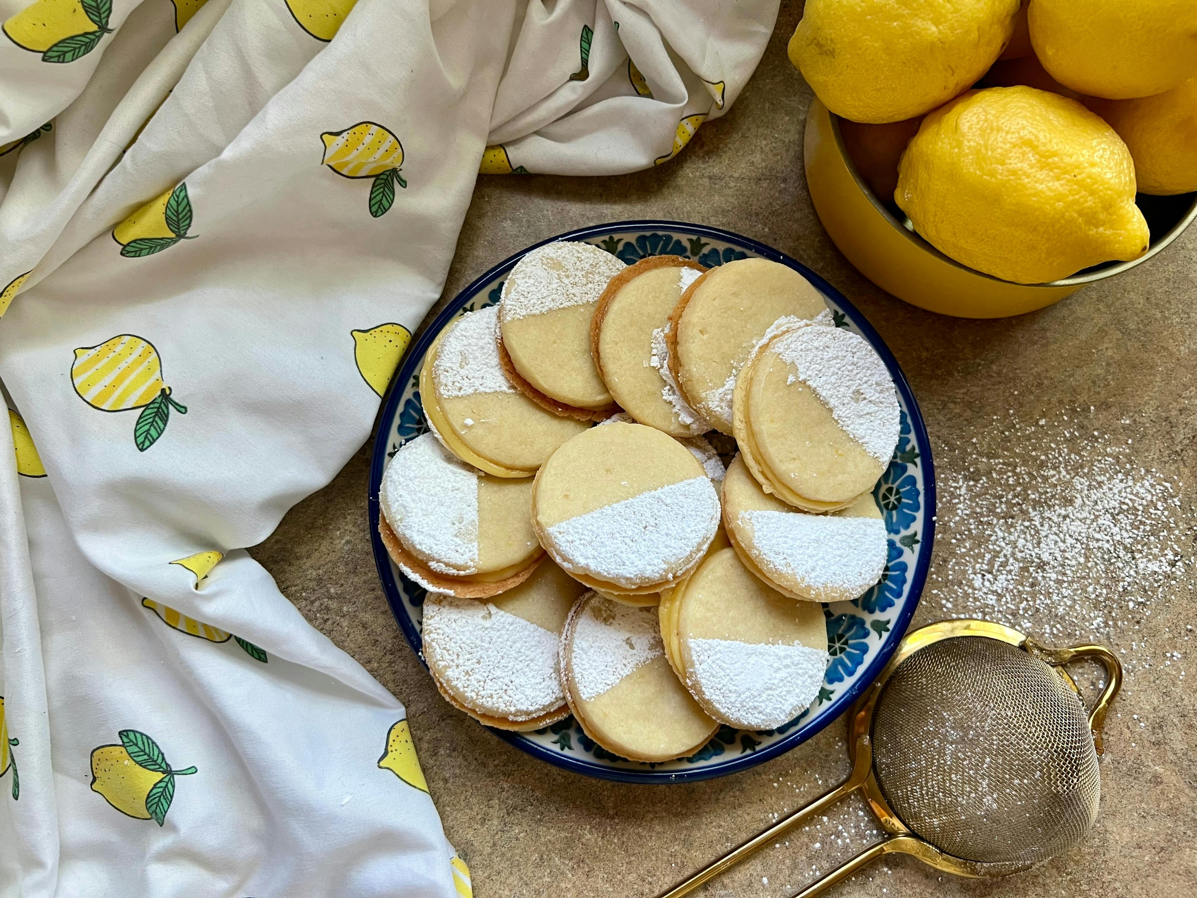 A plate of lemon cookies with a bowl of lemons and lemon fabric.