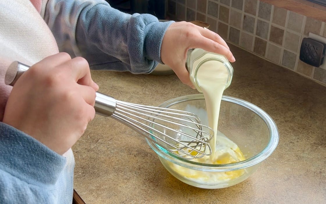 Pouring milk into a bowl with a whisk.
