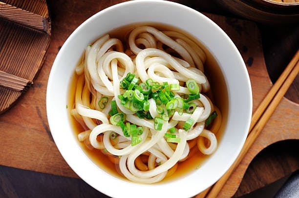 A brothy bowl of thick white udon noodles.
