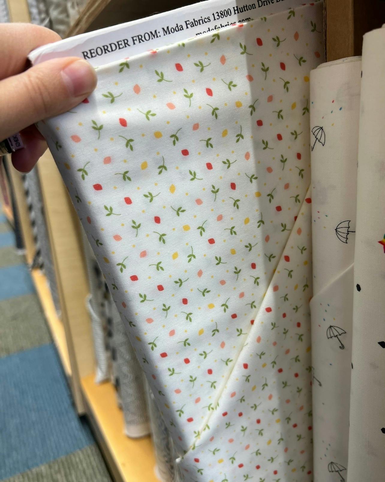 White fabric with tiny green leaves and pink and yellow petals on the shelf at a fabric store.