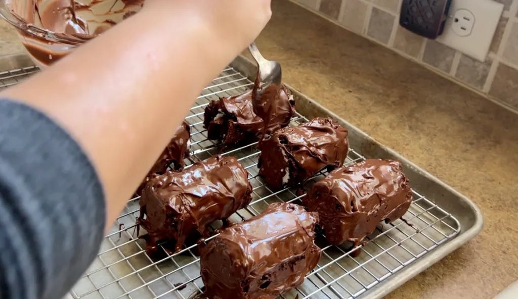 Covering the chocolate mini-rolls in melted chocolate.