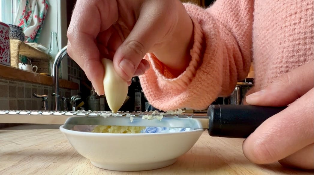 Grating a clove of garlic on a microplane grater.