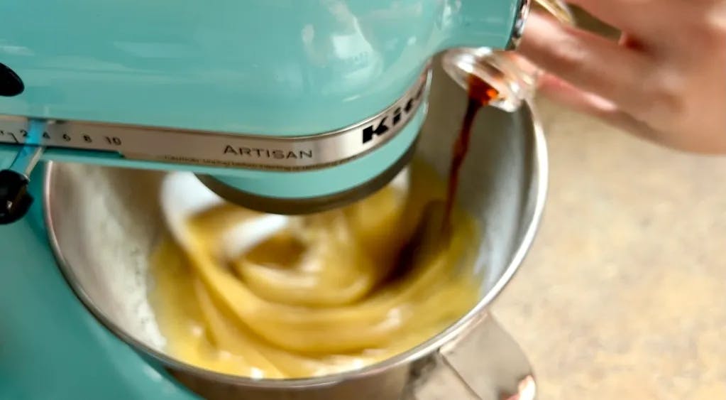 Pouring vanilla into a stand mixer full of batter.