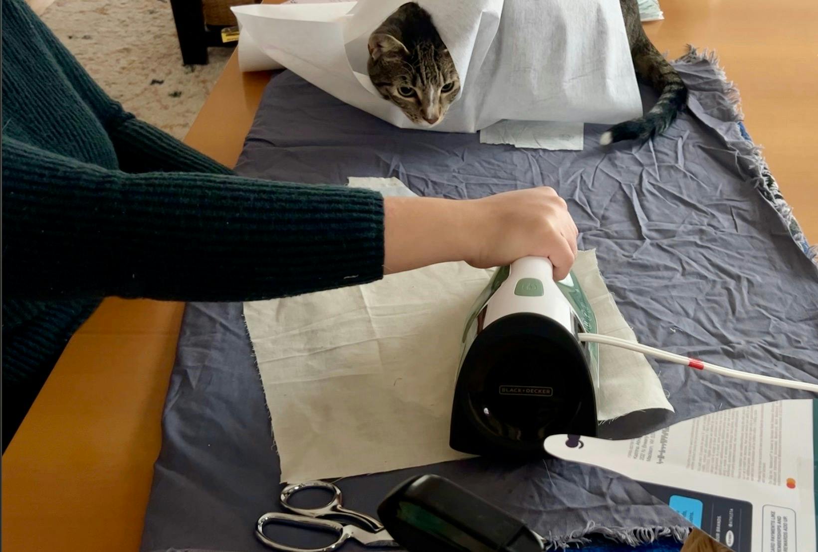 pressing interfacing onto fabric, with Pete watching from a bundle of interfacing.