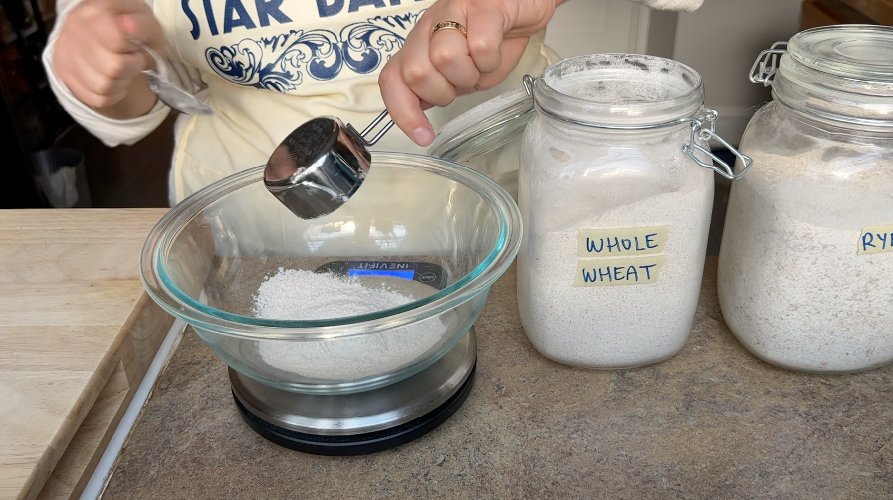 Measuring whole wheat flour into a bowl with a jar of rye flour almost off camera