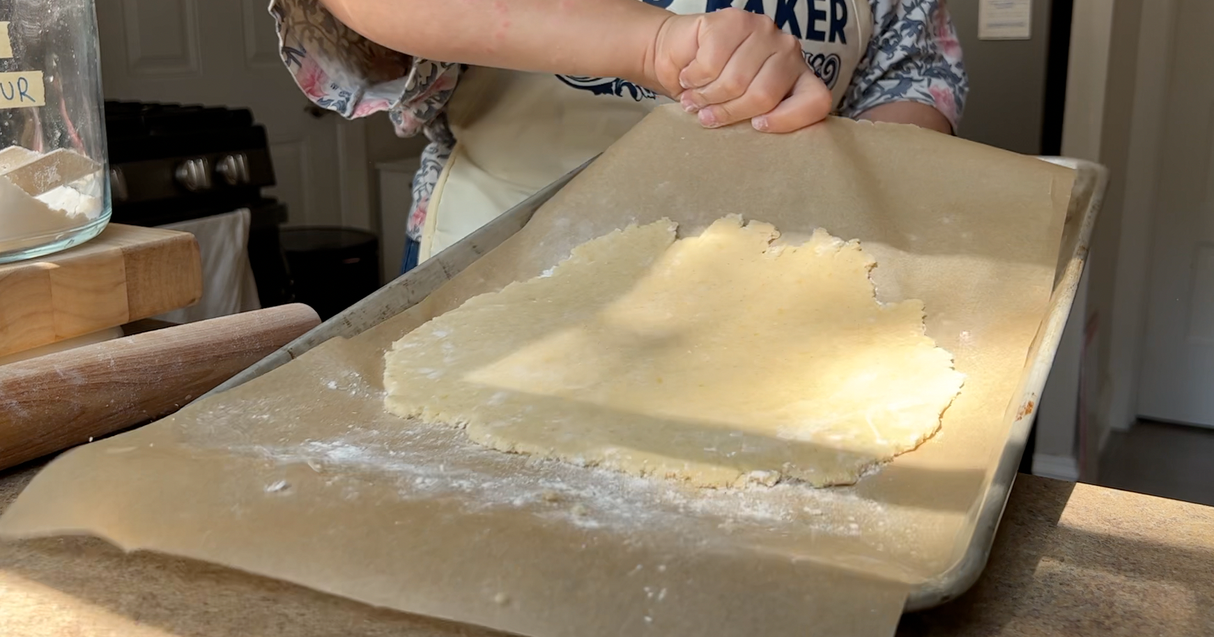 Sliding a piece of parchment paper with a thinly rolled out cookie dough onto a sheet tray.