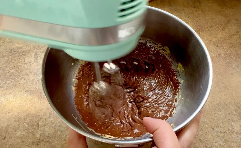 A hand mixer stirring what looks like brownie batter.