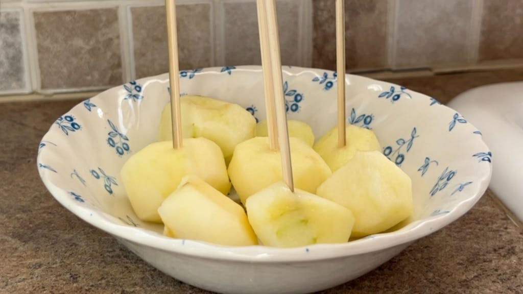 A bowl of raw apple carved into small spheres with skewers sticking out of them.