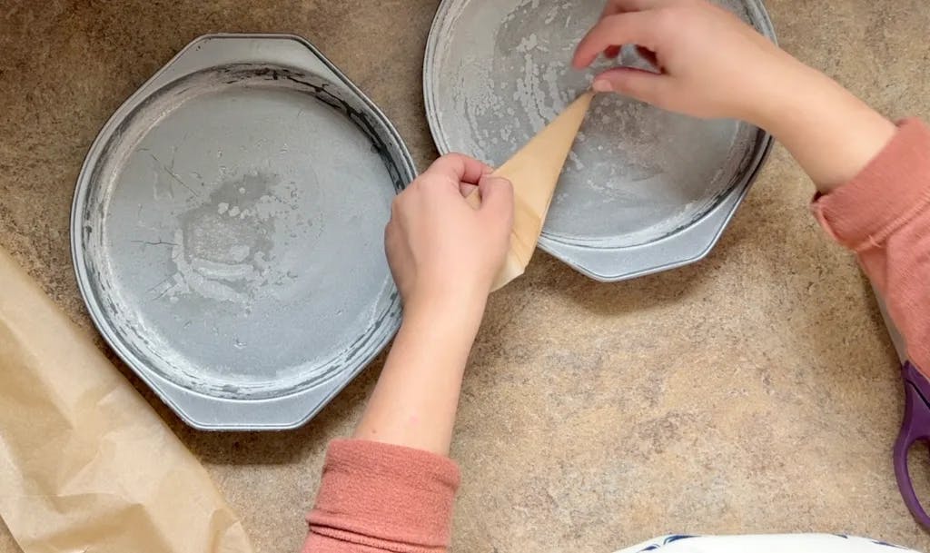 Lining two round cake pans with parchment paper.