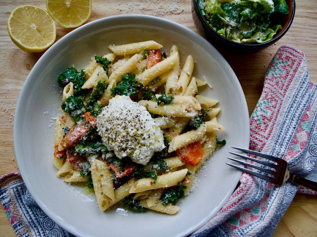 A bowl of pasta and veggies with a dollop of ricotta cheese on top.