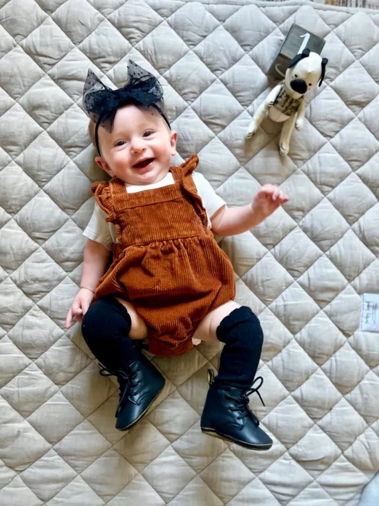 Stella, a baby, lies with the fabric Brexley. She is wearing a brown corduroy romper and is smiling.