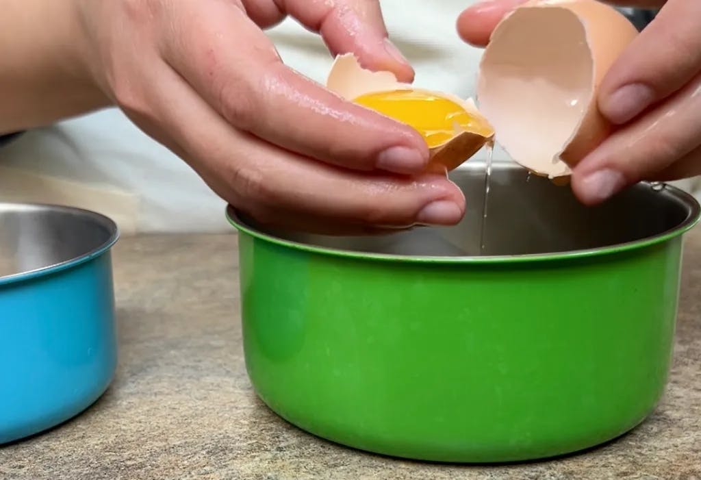 Separating an egg yolk from white into a green bowl.