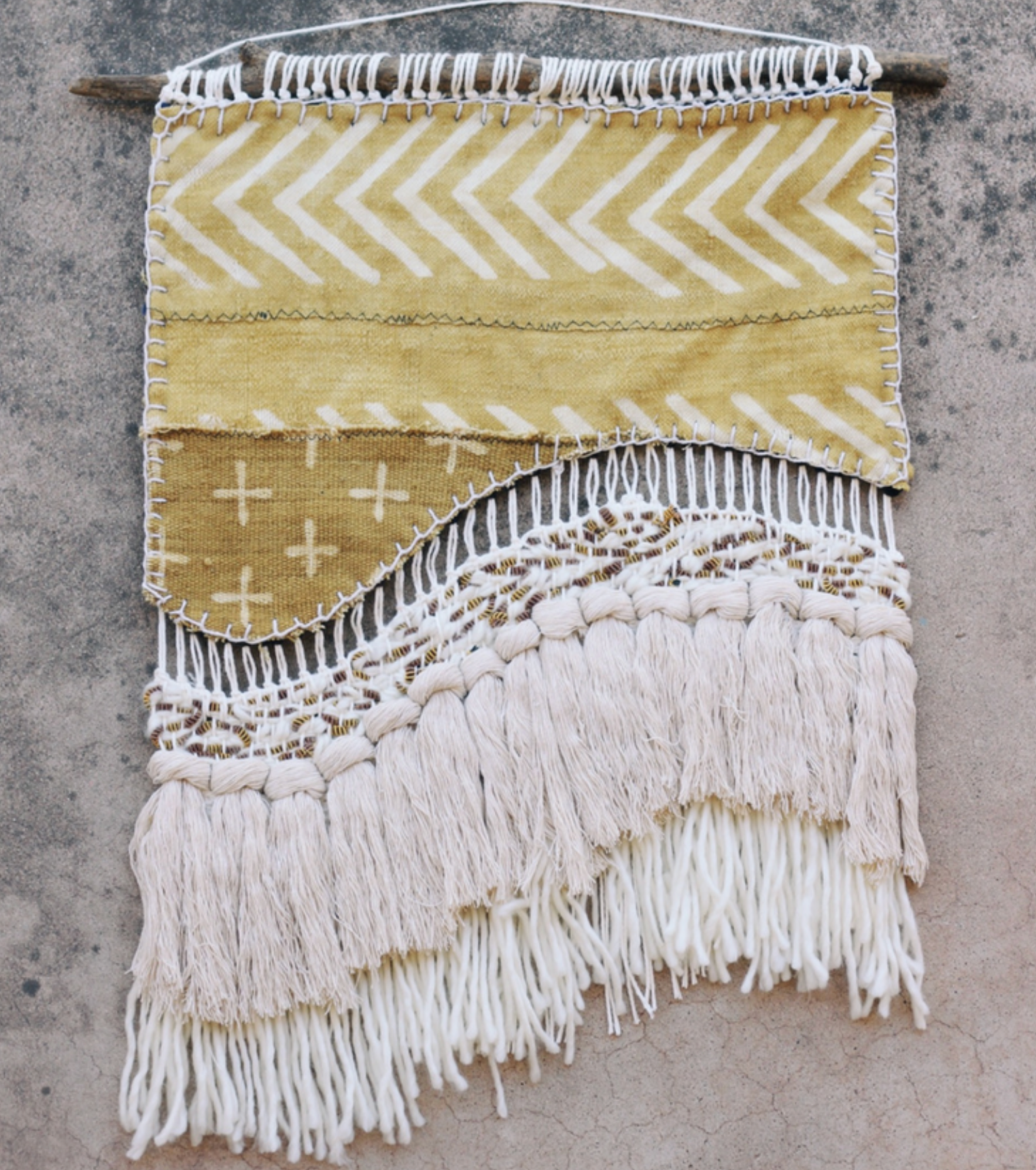 A fabric and yarn wall hanging in yellow and white